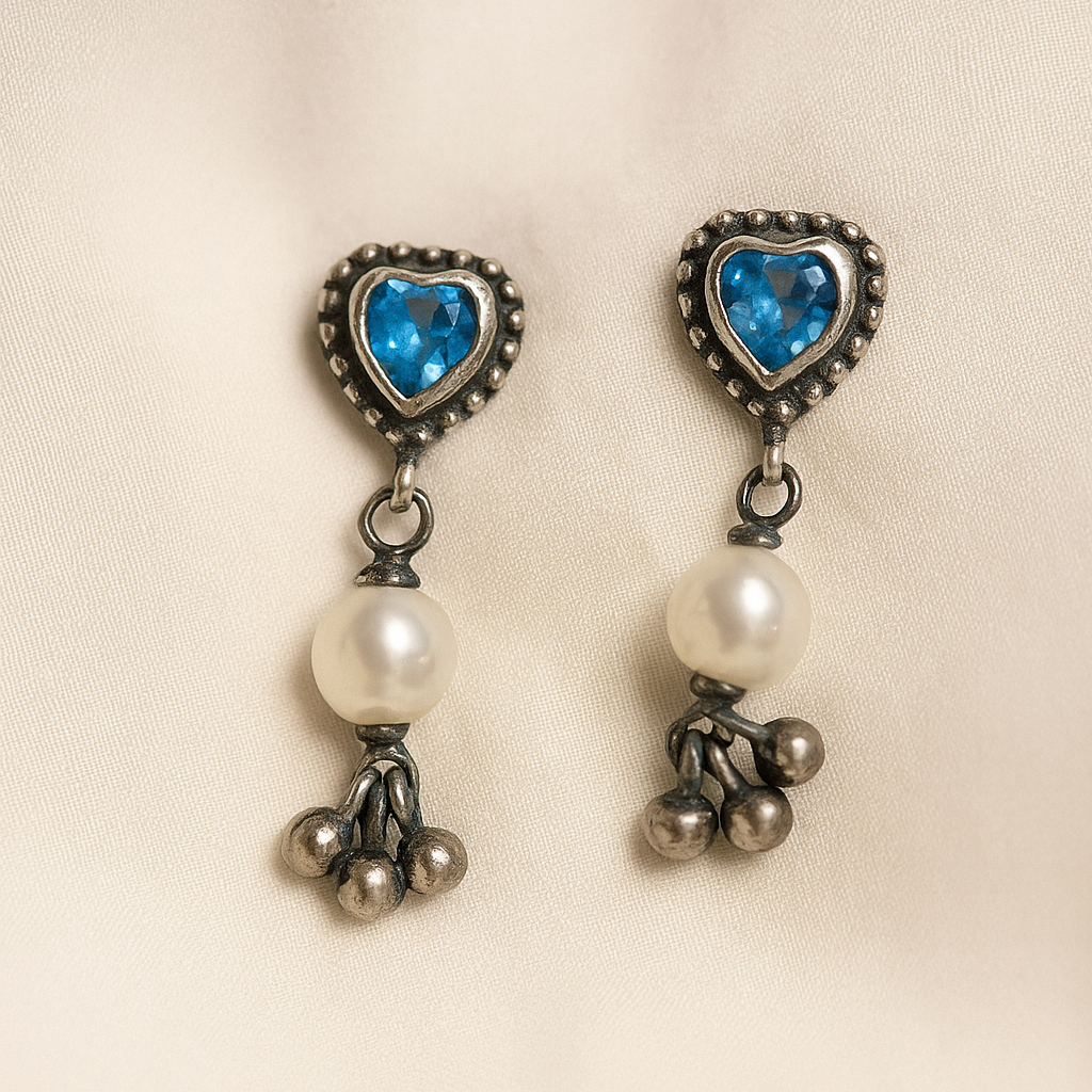Pair of heart-shaped earrings with blue gemstones and pearl-like beads on a beige background