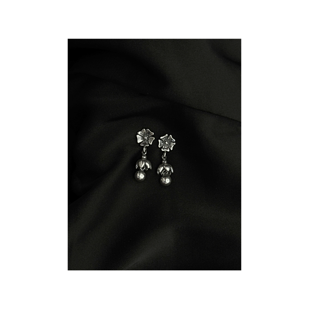 Silver floral earrings on a black fabric background