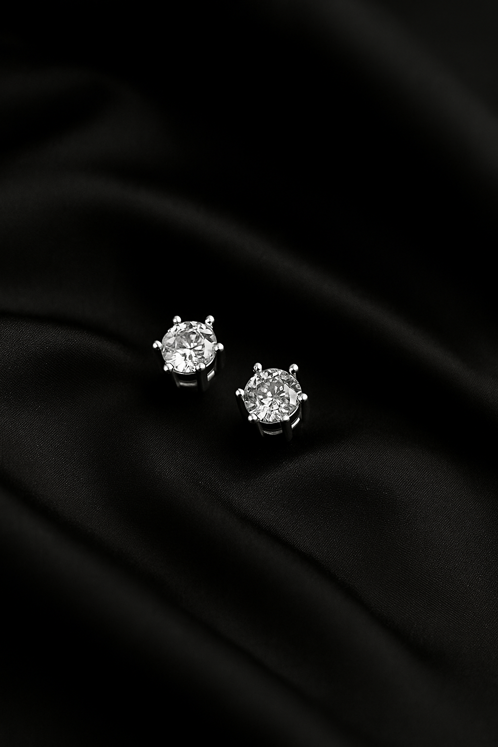 Pair of diamond stud earrings on a black fabric background