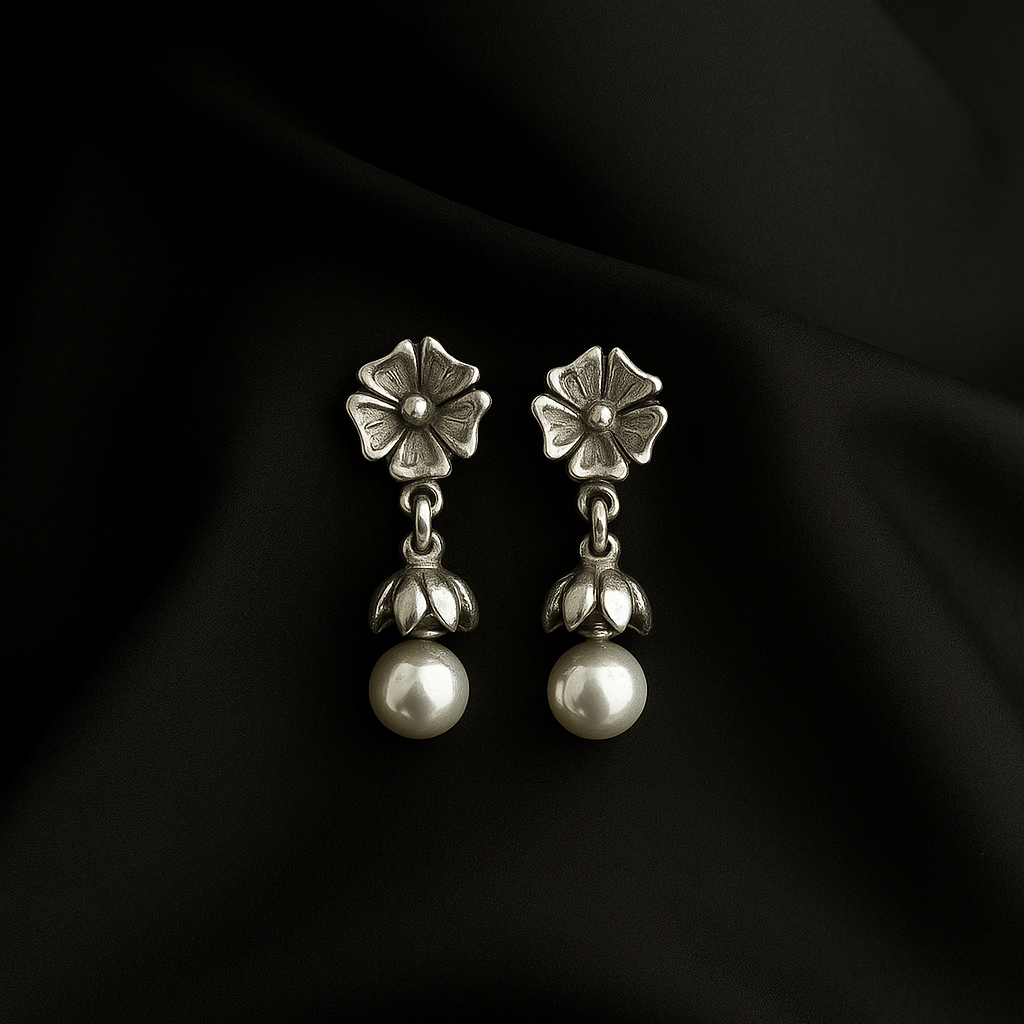 Pair of silver earrings with floral tops and pearl-like bottoms on a black fabric background
