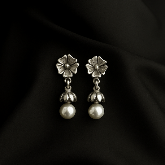Pair of silver earrings with floral tops and pearl-like bottoms on a black fabric background