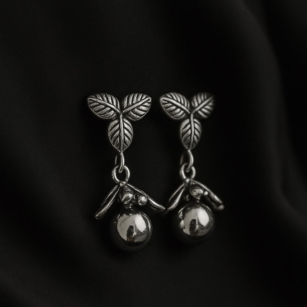 Pair of silver earrings with leaf design on a dark fabric background