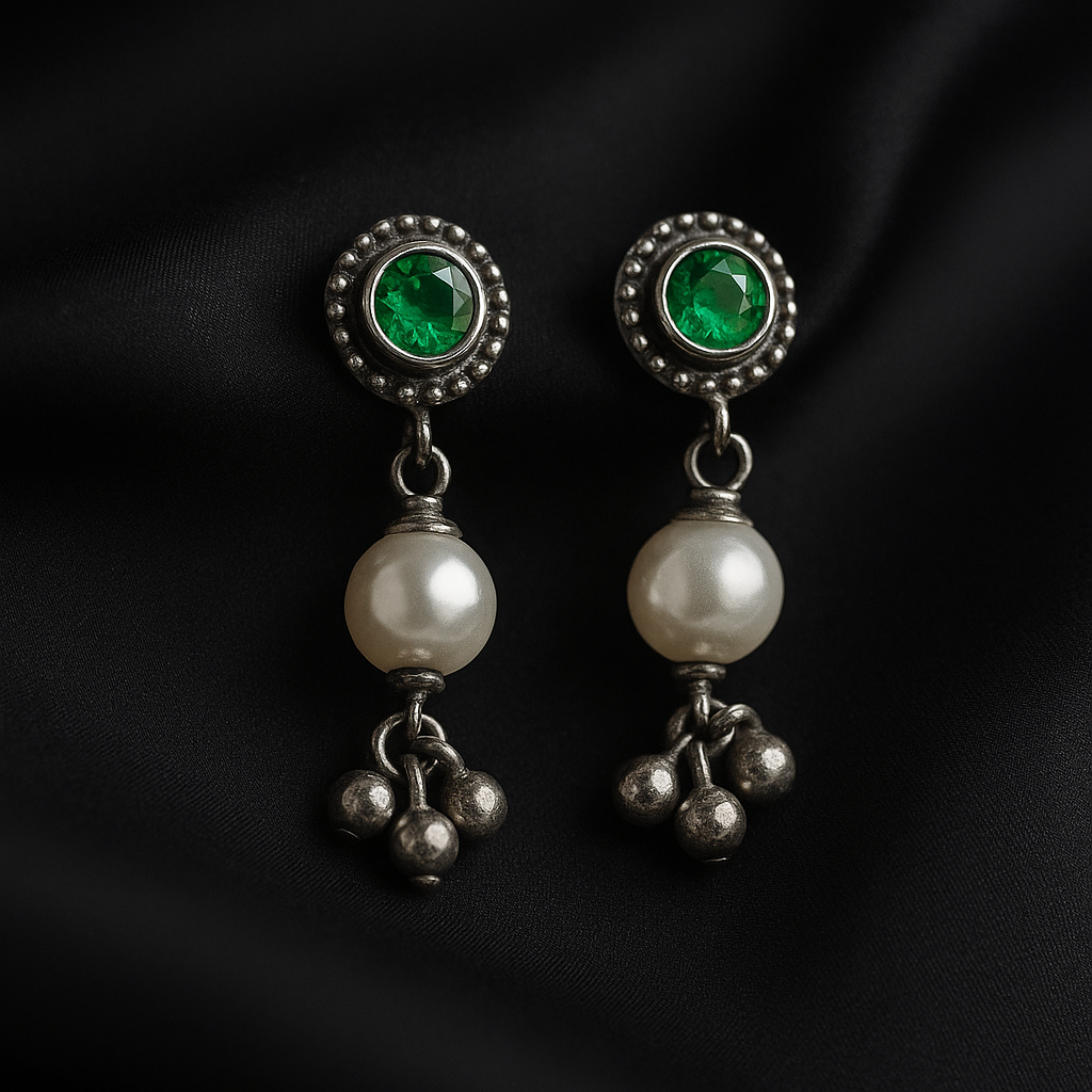 Pair of earrings with green gemstones and pearl-like beads on a black background