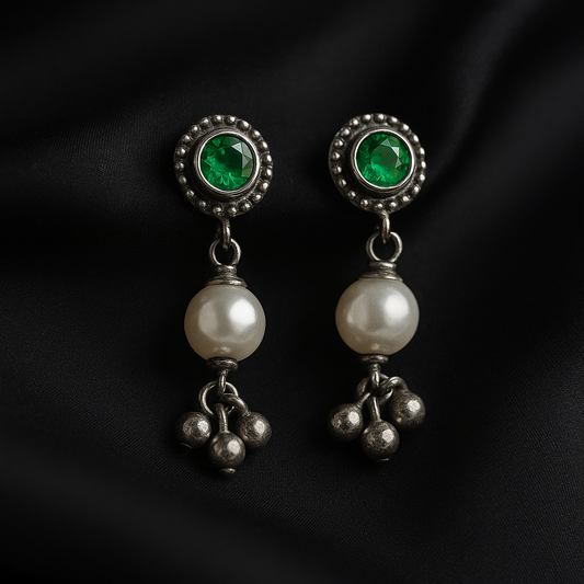 Pair of earrings with green gemstones and pearl-like beads on a black background