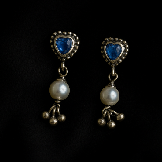 Pair of earrings with heart-shaped blue stones and pearl-like beads on a black background