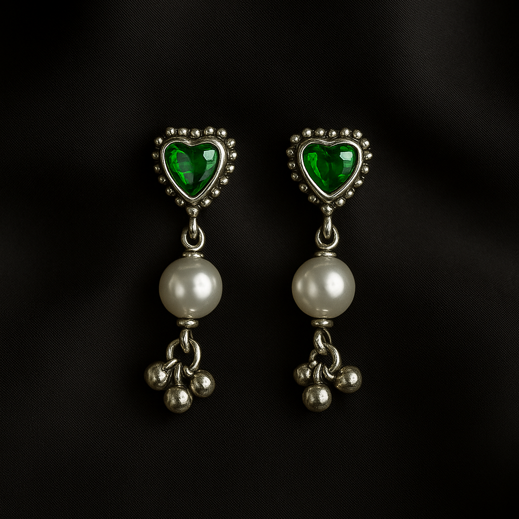 Pair of earrings with heart-shaped green gemstones and pearl-like beads on a black background