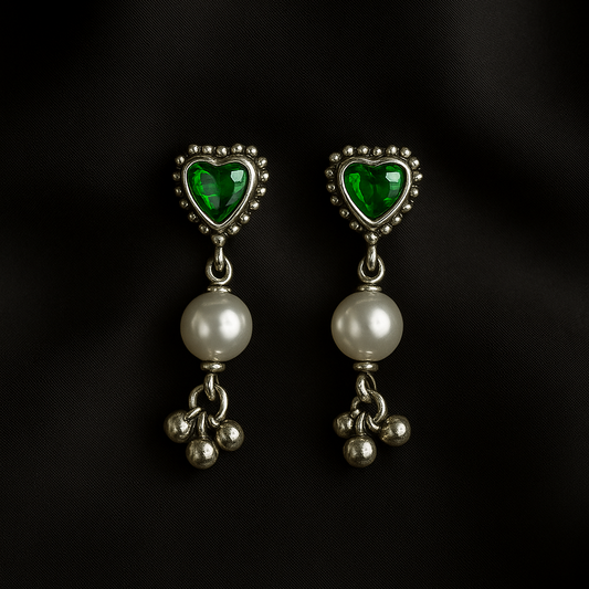 Pair of earrings with heart-shaped green gemstones and pearl-like beads on a black background