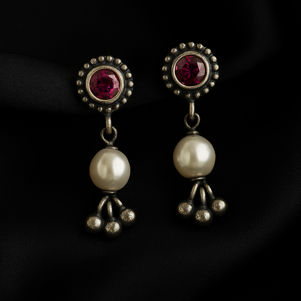 Pair of earrings with red gemstones and pearl-like beads on a dark background