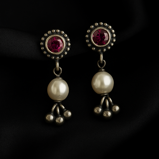 Pair of earrings with red gemstones and pearl-like beads on a dark background