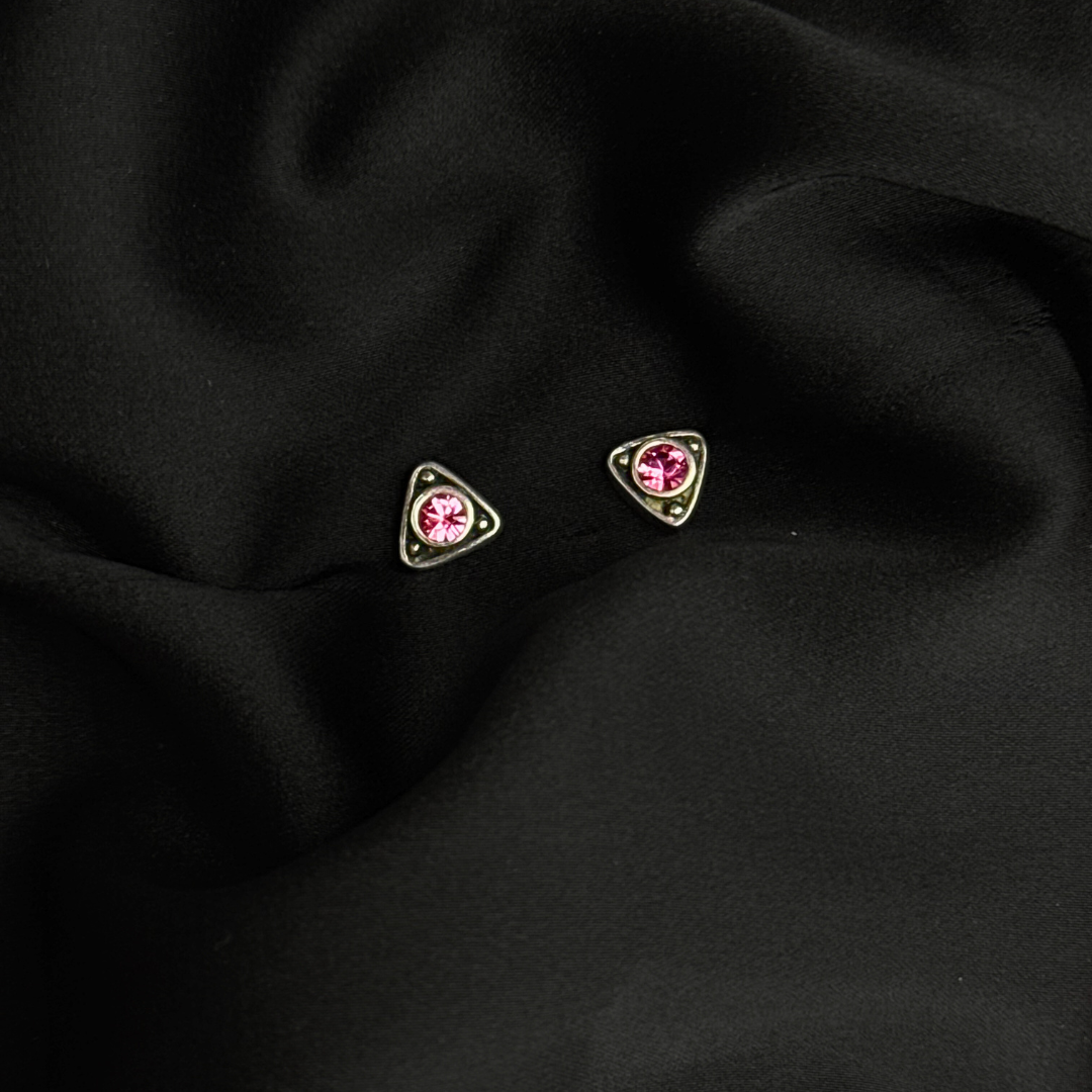 Triangular earrings with pink gemstones on a black fabric background